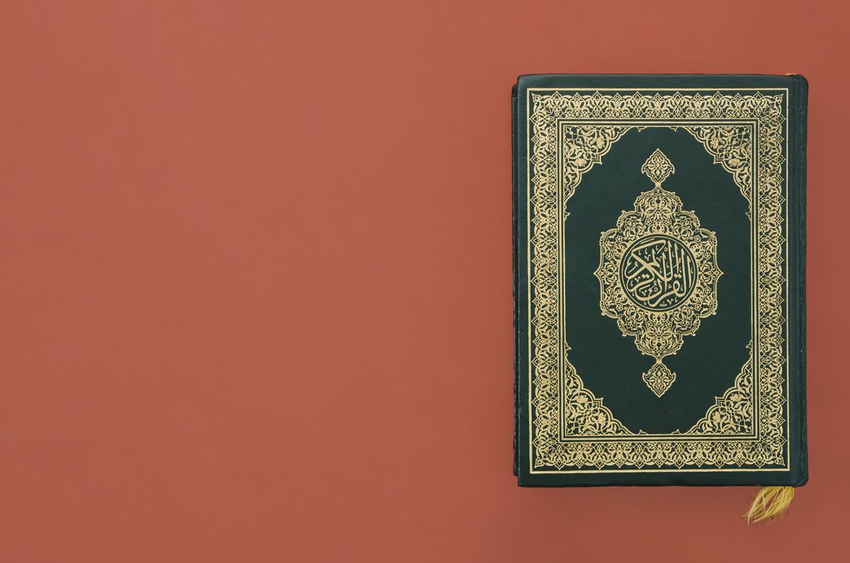 Un mushaf à la couverture verte et dorée posé sur un fond orange